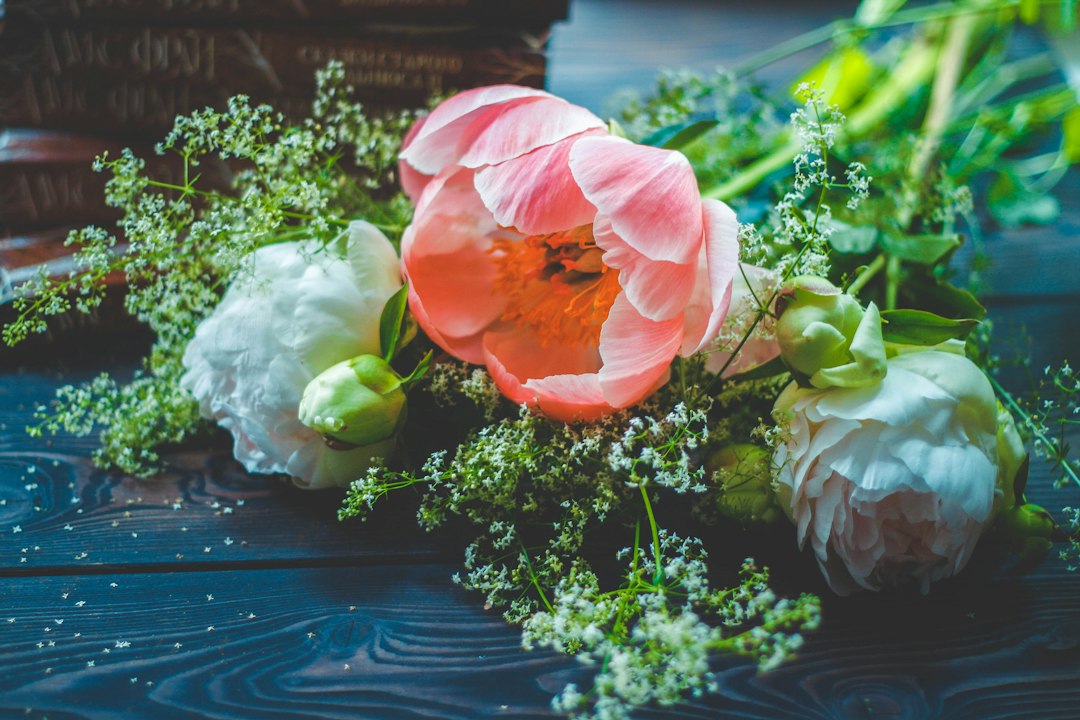 Pink and white peonies with greenery on a dark wooden surface.